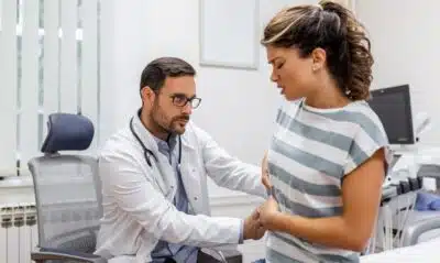 Patient telling physician about her pain and health problems during visit to hospital. Young woman complaining about back or kidney ache while sitting on examination bed at the doctor's office
