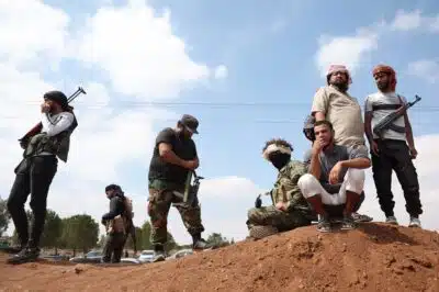 Tribal fighters stand next to a government checkpoint in the town of Busra al-Hariri, east of the city of Sweida, on July 20, 2025, set up to prevent them from advancing towards the city. A ceasefire announced on July 19, appeared to be holding after earlier agreements failed to end fighting between longtime rivals the Druze and the Bedouin that spiralled to draw in the Islamist-led government, the Israeli military and armed tribes from other parts of Syria. (Photo by OMAR HAJ KADOUR / AFP)